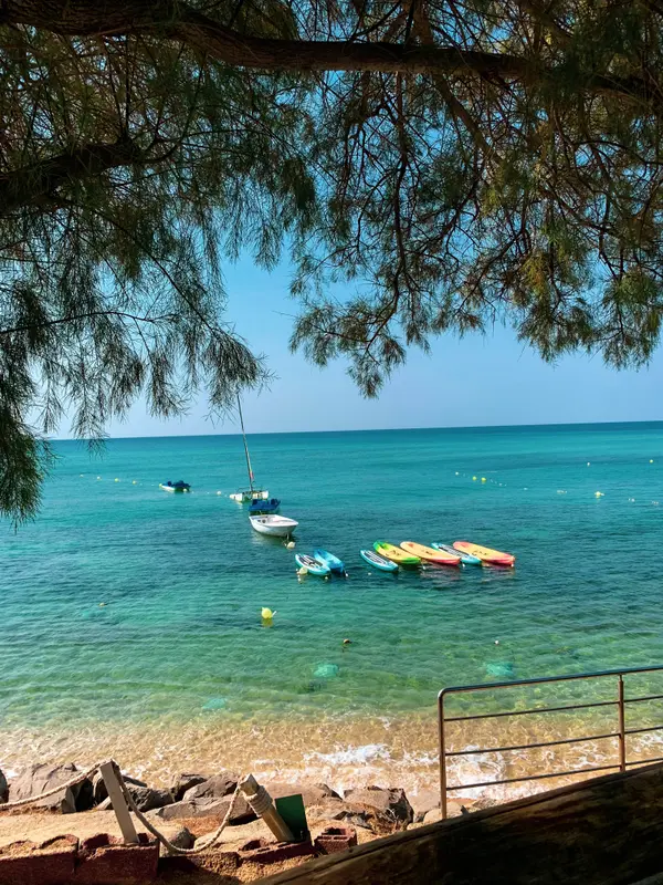 Turquoise sea with colorful kayaks and boats framed by tree branches — Aziz Stiti travel photography