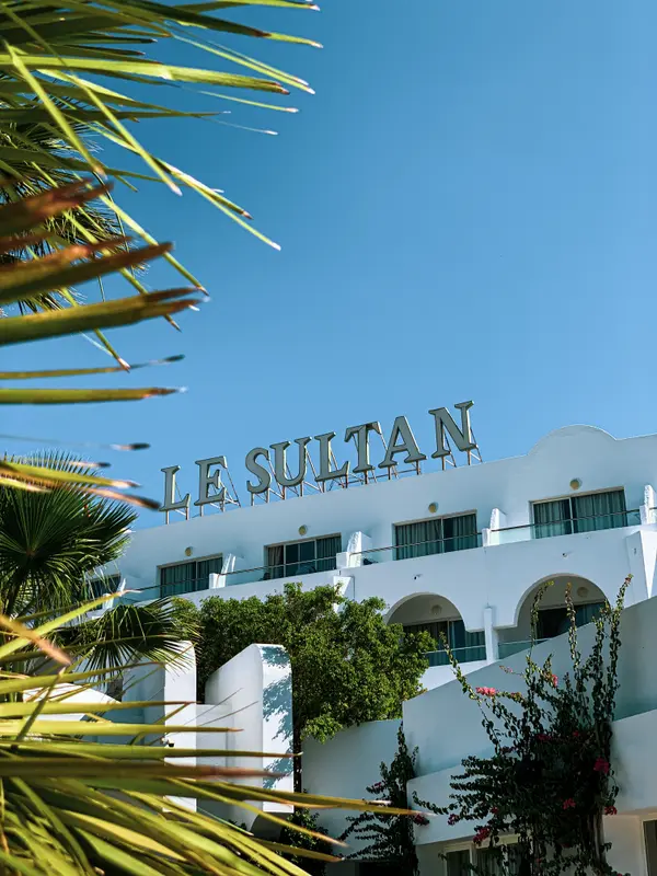 Le Sultan Hammamet white hotel facade with rooftop sign framed by palm leaves — Aziz Stiti
