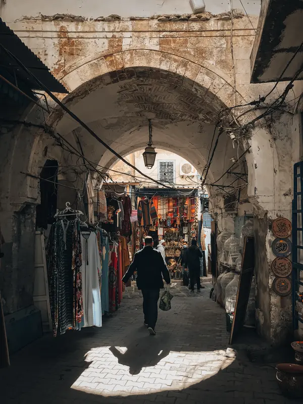 Man walking through a souk archway with sunlight and hanging textiles in Tunis — Aziz Stiti photography