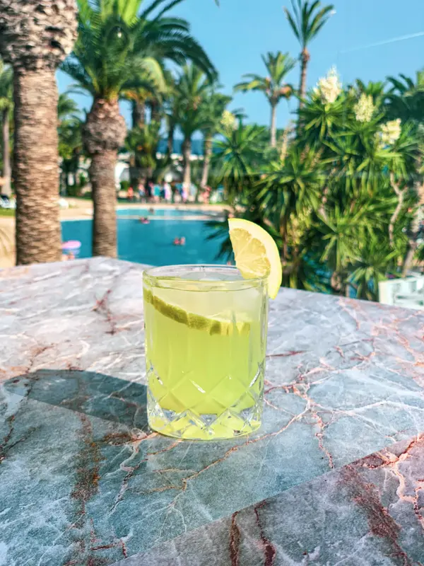 Yellow lemon cocktail on marble table with pool and palm trees in background at TUI Blue — Aziz Stiti